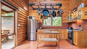 A wooden cabin kitchen with a wooden table, a refrigerator, a stove, and hanging pots. - Stunning holiday home that has you feeling like you are in a Swiss chalet (Blairgowrie)