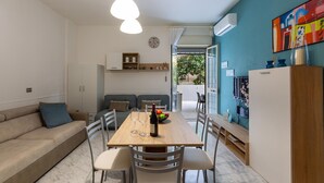 A modern living space with a wooden dining table, white chairs, a beige sofa, and a blue accent wall. - 2517 Villetta Lido La Pineta by Barbarhouse (Gallipoli)