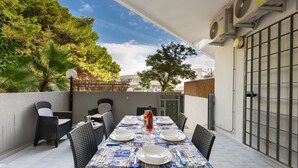 An outdoor patio with a table set for four, surrounded by wicker chairs, and air conditioning units on the wall. - 2517 Villetta Lido La Pineta by Barbarhouse (Gallipoli)