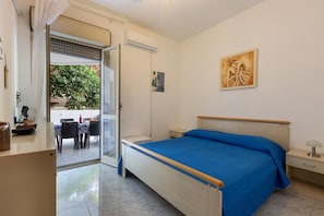 A bedroom with a bed, a nightstand, a desk, a chair, and a window with a view of greenery outside. - 2517 Villetta Lido La Pineta by Barbarhouse (Gallipoli)