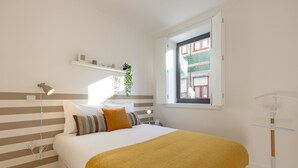 A neatly arranged bedroom with a bed, bedside table, lamp, and a window with a view of buildings. - Sweet Flat 4Two in City Center w/ Balcony & Air Conditioning (Porto)