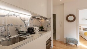 A modern kitchen with a marble countertop, stainless steel sink, and a compact dining area with a small table and bench. - Sweet Flat 4Two in City Center w/ Balcony & Air Conditioning (Porto)