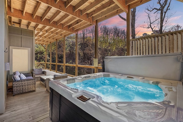 Un bain à remous situé dans un espace extérieur abrité, agrémenté de poutres en bois, de meubles en osier et offrant une vue sur les arbres et le ciel.