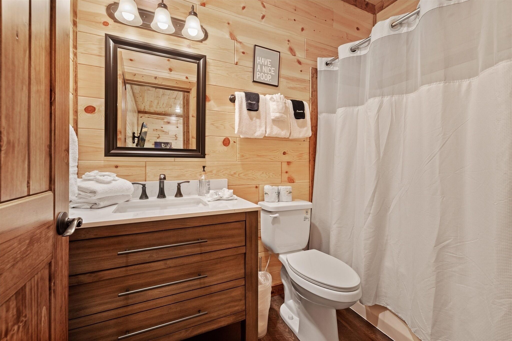 Ein Badezimmer mit Holzpaneelen, einem Waschbecken, einem Spiegel, einem Handtuchhalter, einer Toilette und einer Duschvorhang.