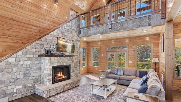 A spacious living area with a stone fireplace, wooden ceiling, and a large couch. - Smokey Treats 5 Bedroom Cabin by RedAwning (Gatlinburg)