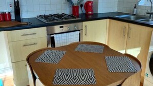 A modern kitchen with a round wooden table, four chairs, a gas stove, a coffee machine, and a washing machine. - Central Taunton 2-bedroom apartment, great views! (Taunton)