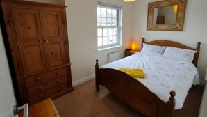 A bedroom with a wooden wardrobe, a bed with white linens, a bedside lamp, and a window with blinds. - Central Taunton 2-bedroom apartment, great views! (Taunton)