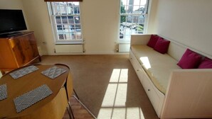 A small, well-lit room with a sofa, a television, and a table with patterned placemats. - Central Taunton 2-bedroom apartment, great views! (Taunton)
