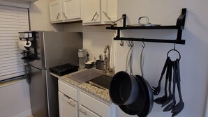 Uma cozinha com armários brancos, uma geladeira de aço inoxidável, um suporte de panelas preto suspenso e um piso revestido de azulejos.
