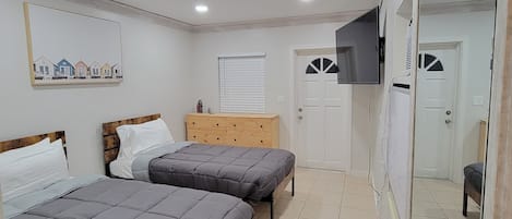 Un dormitorio con dos camas, un aparador de madera, una puerta blanca y un espejo grande.