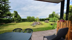 Een terras met een tafel en stoelen, een houten omheining en een stapel hout in een tuin.