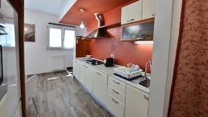 Een kleine keuken met witte kastjes, een gasfornuis, een spoelbak en een raam.