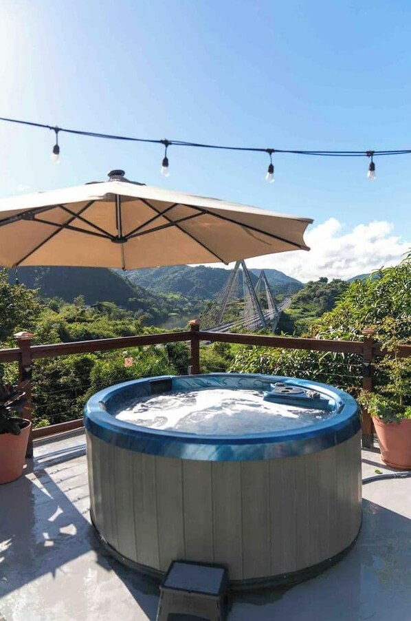 A hot tub on an outdoor terrace with a view of mountains and a bridge.