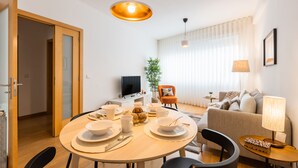 A modern living room with a sofa, a dining table set with plates and cups, a TV, and a lamp. - Modern 2BR Apart w/ AC and Parking in City Center (Porto)
