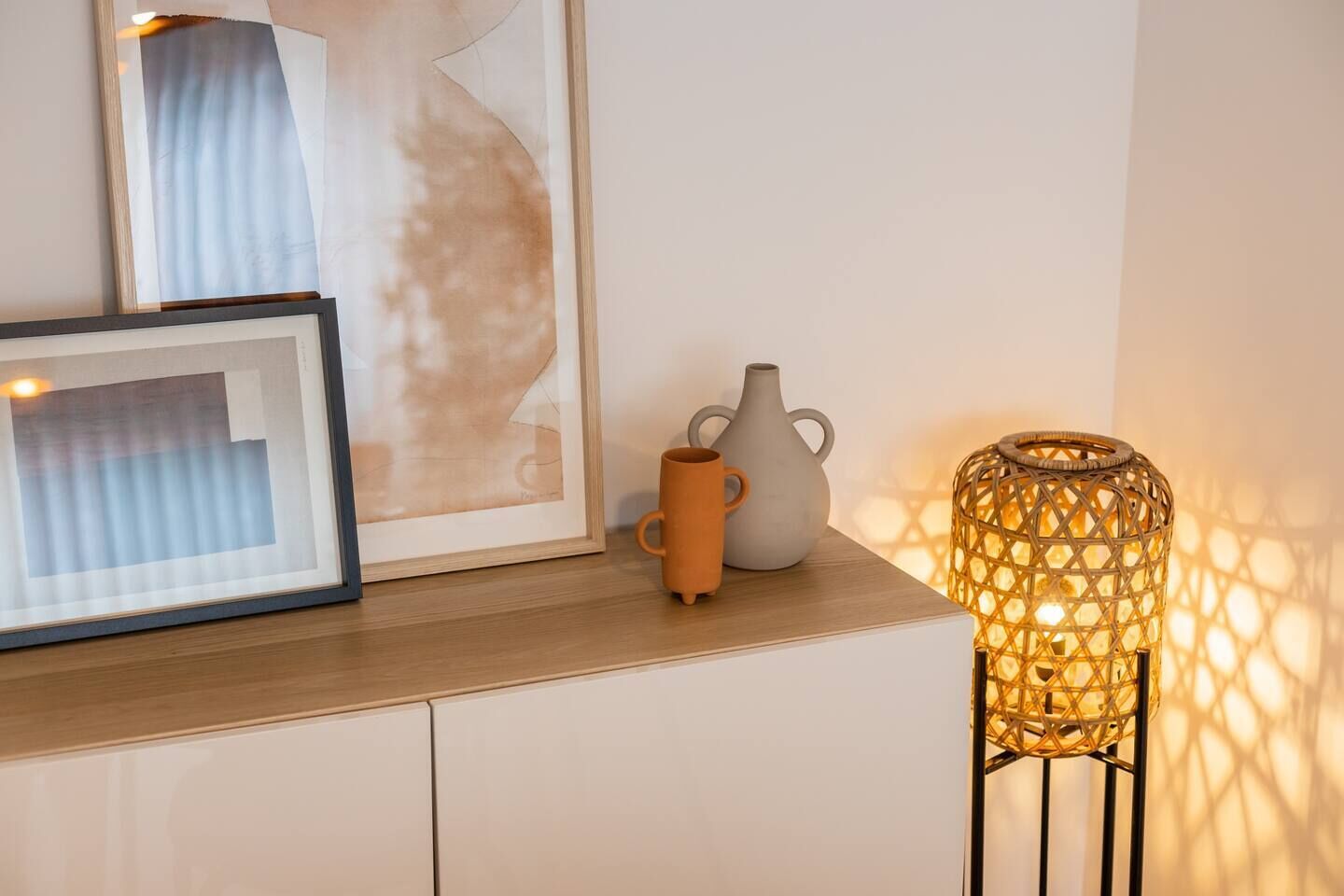 Un tableau abstrait encadré, un vase en céramique et une lampe en osier, le tout posé sur une surface en bois.
