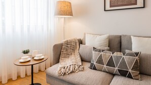 A living room with a sofa, a lamp, a small table with cups and a pitcher, and a framed picture on the wall. - Modern 2BR Apart w/ AC and Parking in City Center (Porto)
