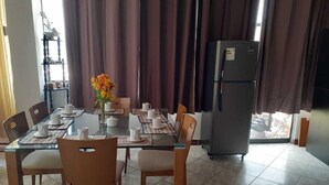 Zona de menjador amb taula de vidre, cadires i un frigorífic.