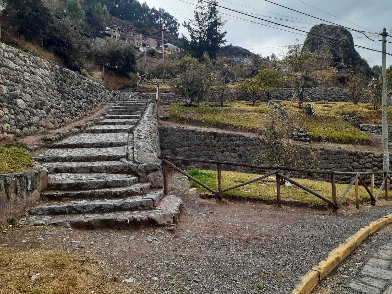 A stone staircase leading uphill with a metal railing, surrounded by a stone wall and vegetation.