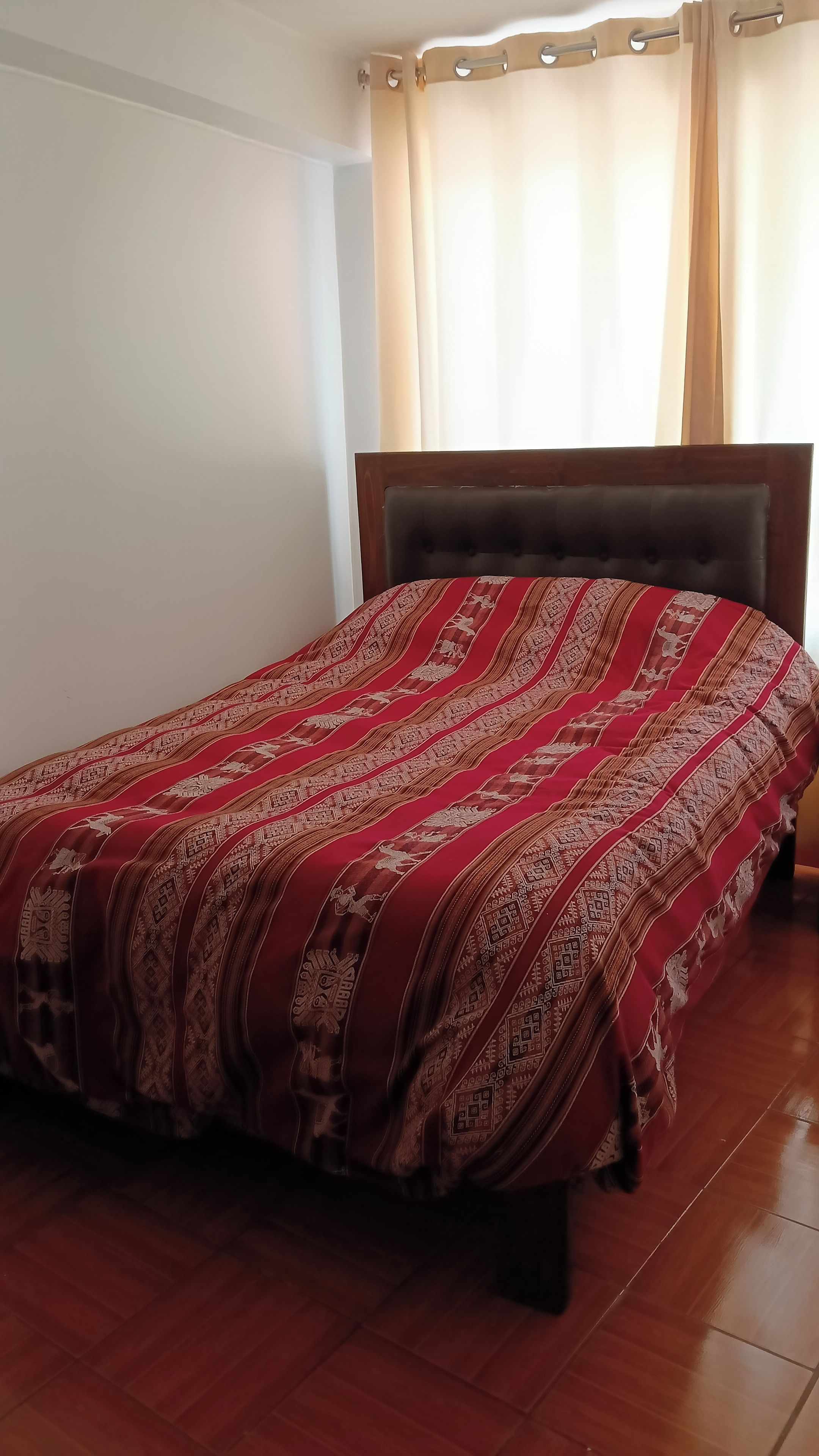 Una cama con una colcha estampada, un cabecero de madera y una ventana con cortinas.
