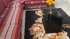 Un saló amb un sofà vermell, una taula de cafè negra amb un disseny floral, i una cuina al fons.