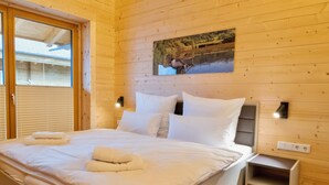 Ein Schlafzimmer einer Holzhütte mit einem Bett, weißer Bettwäsche, einem Nachttisch und einem Bild einer Seenlandschaft.