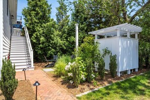 Un jardin à l’arrière de la maison, agrémenté d’une pergola blanche, d’un chemin en briques et d’un petit espace paysager avec des fleurs et des arbustes blancs.