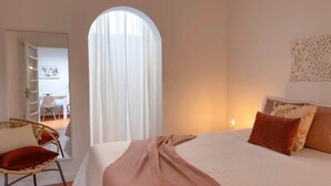 Un dormitorio con cama, una silla, un ventanal y una pared decorada.