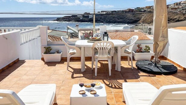 Una terraza con una mesa y sillas, una planta en maceta y vistas al océano y edificios.