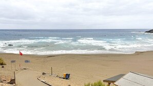 Una playa con un puesto de salvavidas, una bandera y un bote de basura.