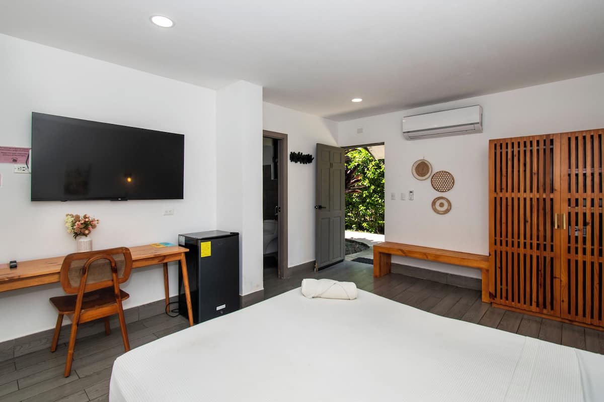 Habitación de hotel con cama, escritorio, silla, televisión, aire acondicionado y vistas al exterior.