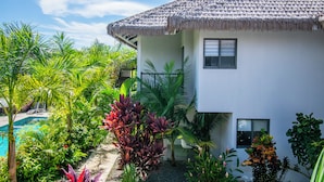 A modern house with a thatched roof, surrounded by lush tropical plants and a swimming pool.
