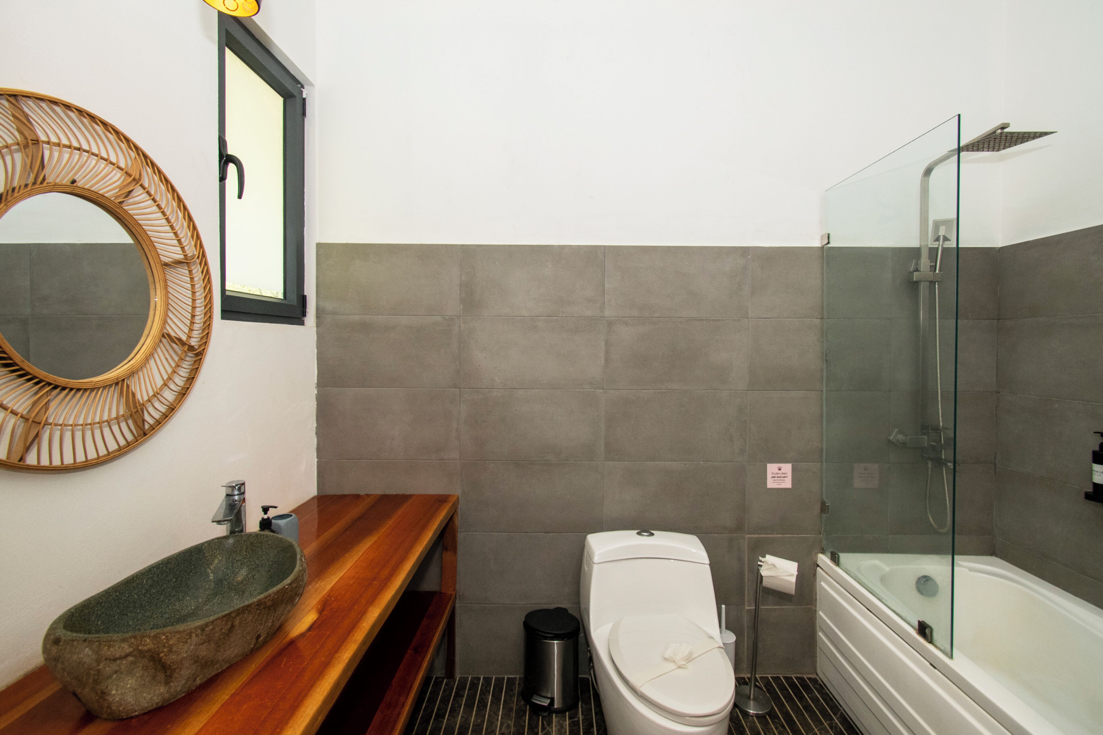 Ein Badezimmer mit einem Steinsink, einer Holzausstattung, einer Toilette, einer Duschkabine aus Glas und einem Spiegel mit Holzrahmen.