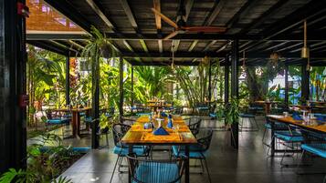 Un restaurant intérieur, doté de tables et de chaises, entouré de plantes et agrémenté d’un plafond en bois.