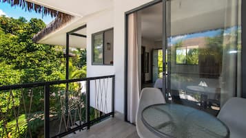 Un balcon avec une porte vitrée, une table ronde et des chaises, donnant sur un jardin luxuriant.
