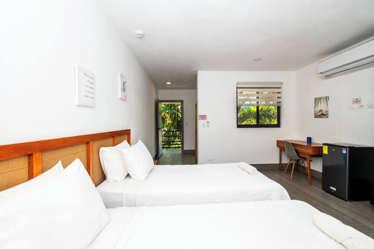 Habitación de hotel con dos camas, un escritorio, una silla, un refrigerador y una ventana con vista a zonas verdes.