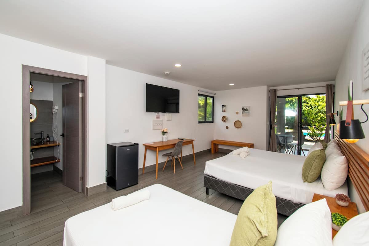 Habitación de hotel con cama, escritorio, silla, televisor y balcón con vistas.