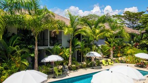 A pool area with umbrellas, lounge chairs, and palm trees.