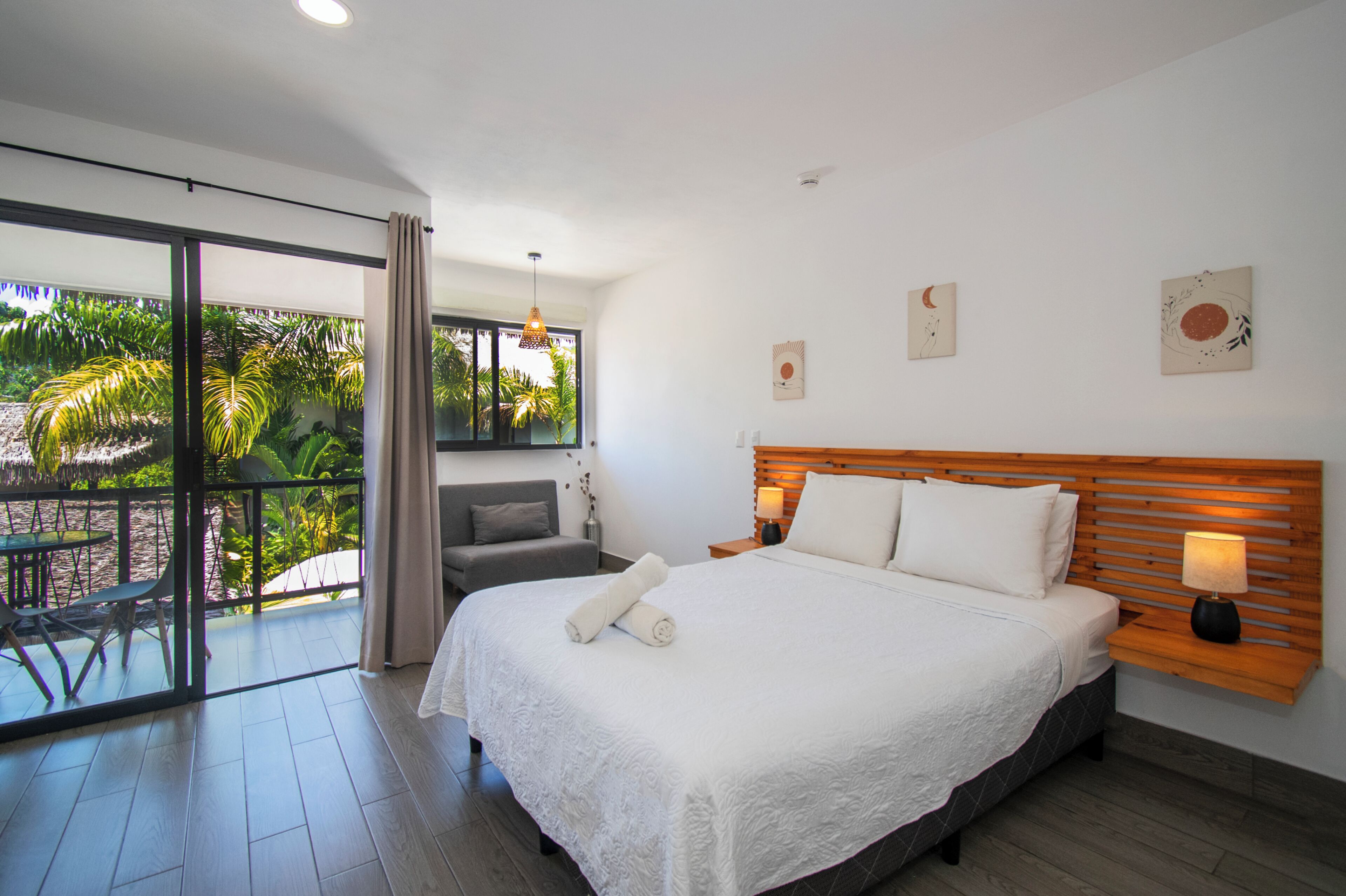 Ein Hotelzimmer mit einem großen Bett, einem Sofa, einem Balkon mit Blick auf Palmen und einer Schiebeglastür.