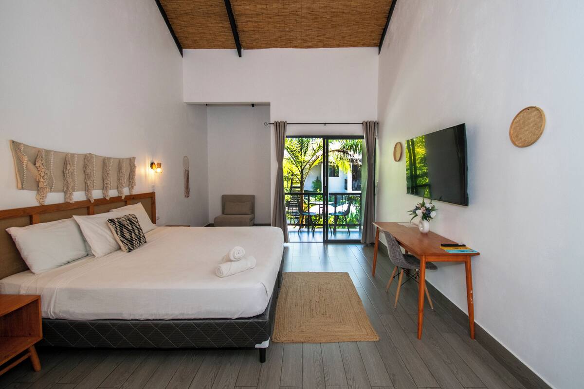 Un dormitorio con cama, escritorio, televisor y vistas al exterior.