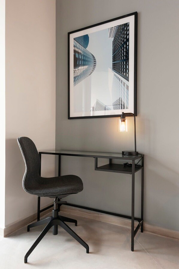 Ein moderner Schreibtisch mit Stuhl, einem gerahmten Bild von Gebäuden und einer Schreibtischlampe.