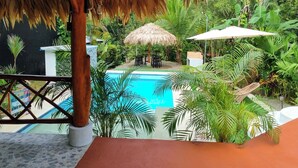 A pool area with a thatched roof, lounge chairs, and tropical plants. - Waitys House (Puertoviejo)