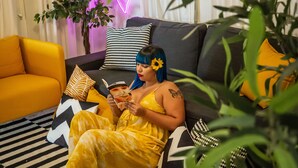 A person sitting on a sofa with a striped rug, surrounded by pillows and a potted plant. - Bed&breakfast, Wifi, Balcony, Jacuzzi, View, Cinema. (Toa Alta)