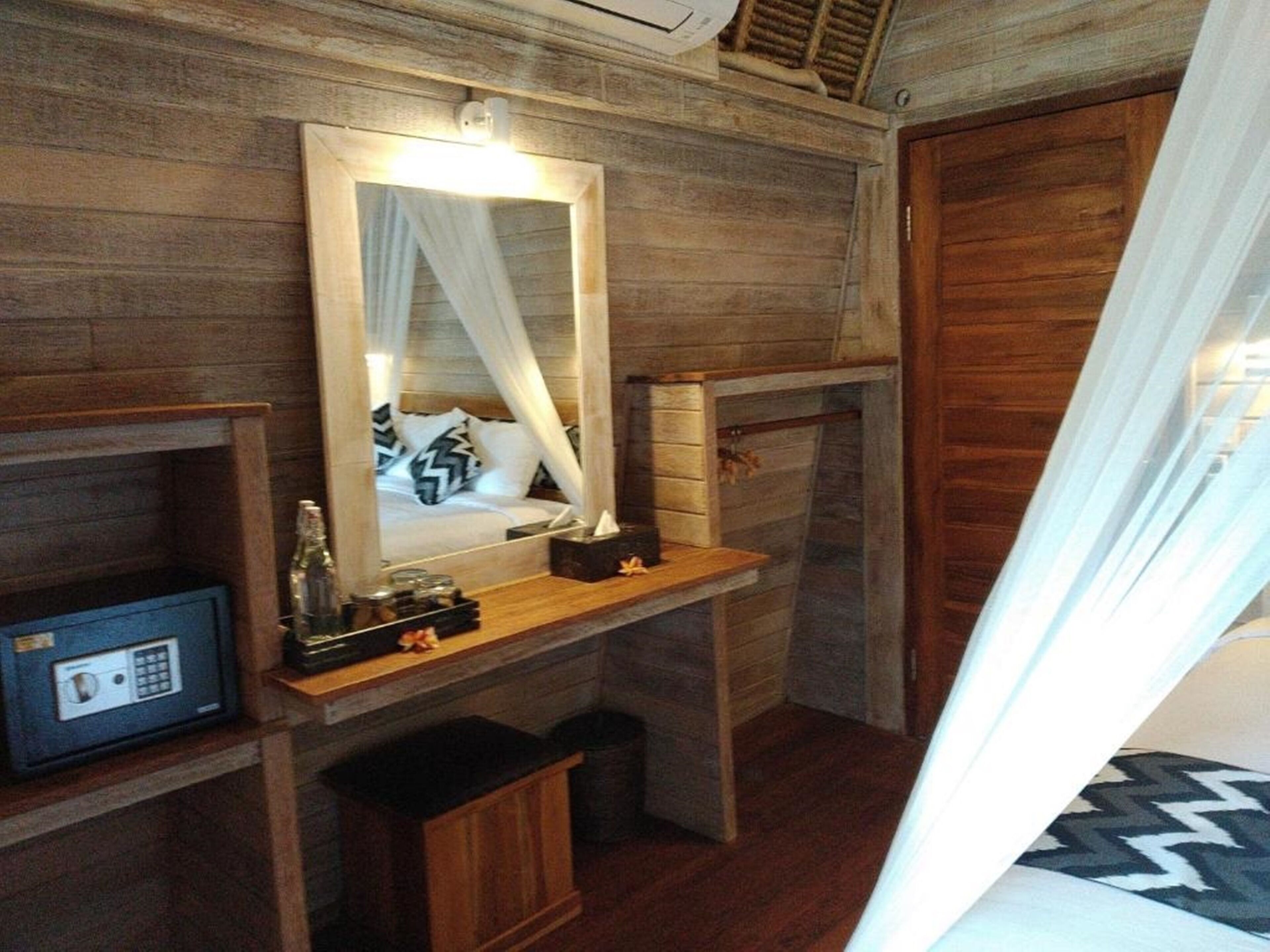 Ein Zimmer aus Holz mit einem Bett, einem Nachttisch, einem Spiegel, einem Safe und einem Vorhang.