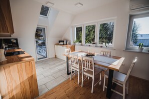 A modern kitchen with a wooden countertop, white chairs, and a dining table. There are potted plants on the windowsill and a skylight above the kitchen.