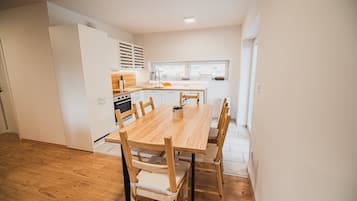 A modern kitchen with a wooden table and chairs, white cabinets, and a window providing natural light.
