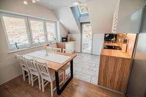 Cozinha moderna com mesa e cadeiras de madeira, forno embutido e vista para o exterior através de grandes janelas.