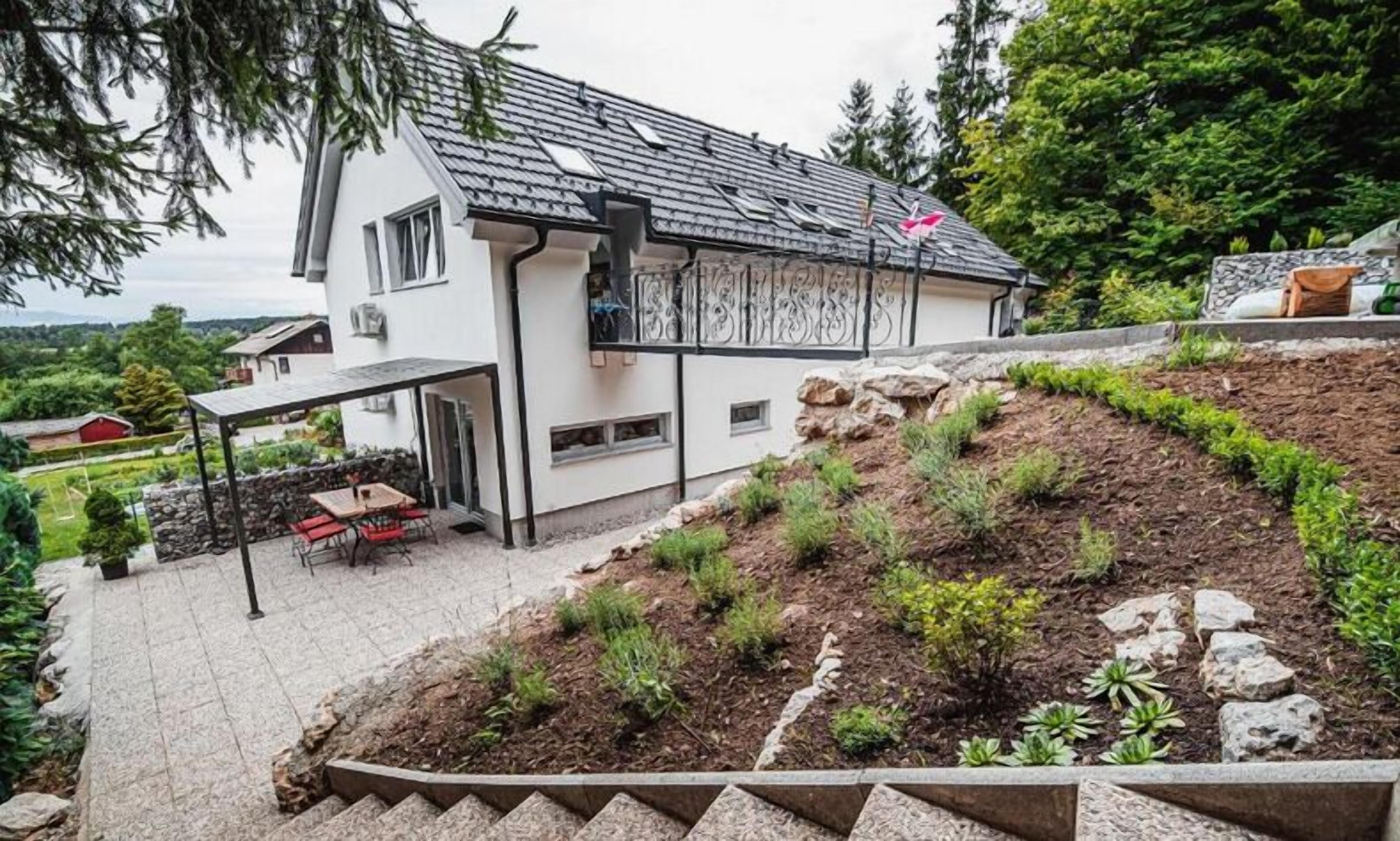 A two-story house with a covered patio, a stone retaining wall, and a landscaped garden.