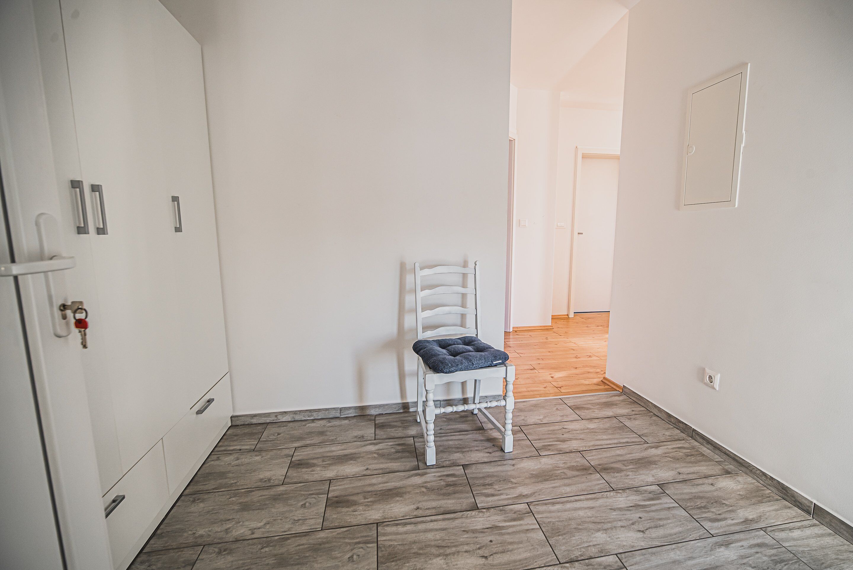 Ein Flur mit einem weißen Stuhl, einem Kleiderschrank und einer Tür mit Schlüsselschloss.