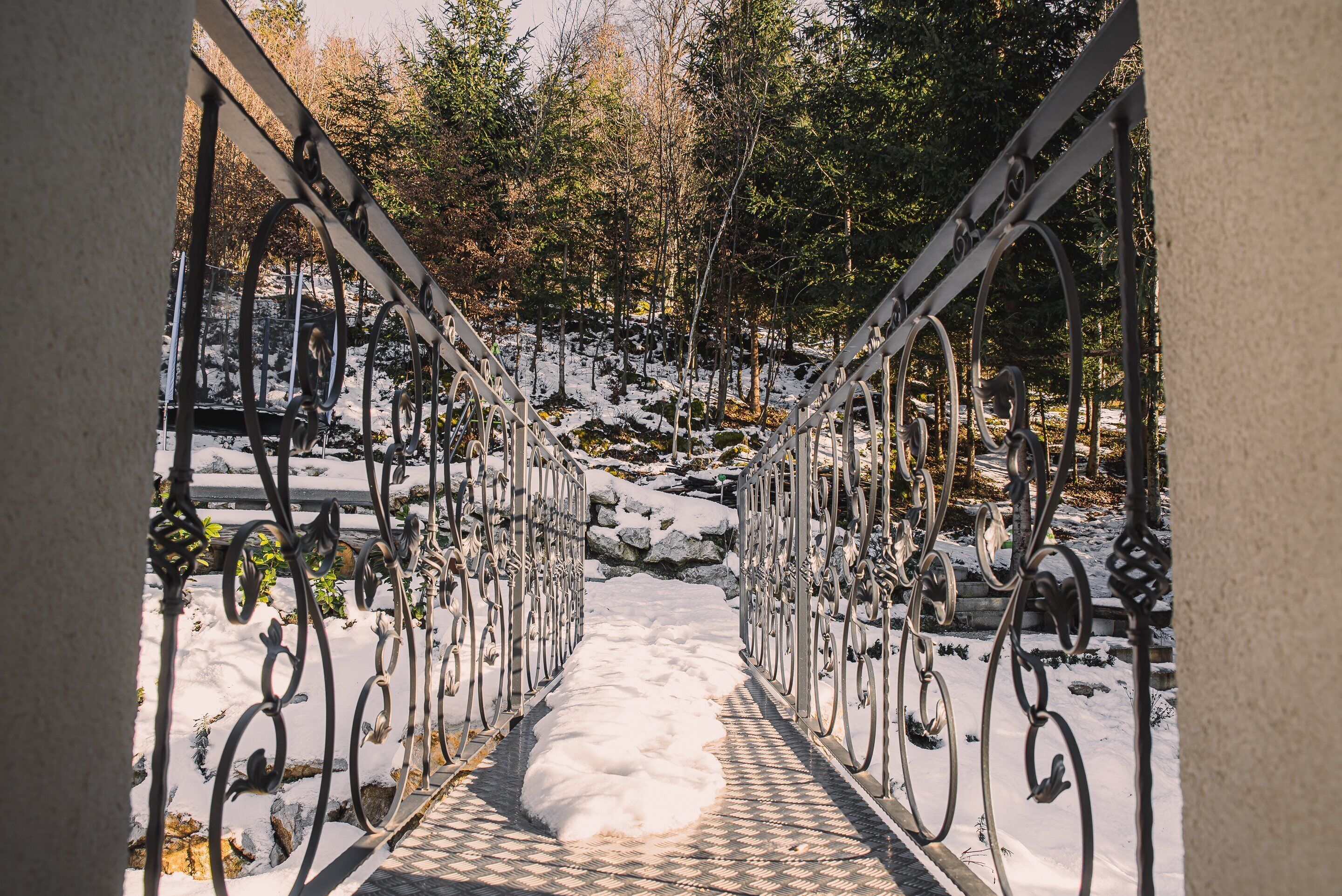 A snow-covered pathway with ornate metal railings leading through a wooded area.