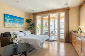 Habitación de hotel con cama, una mesita con un jarrón de flores, un cuadro en la pared y una puerta corredera que da a un espacio al aire libre.